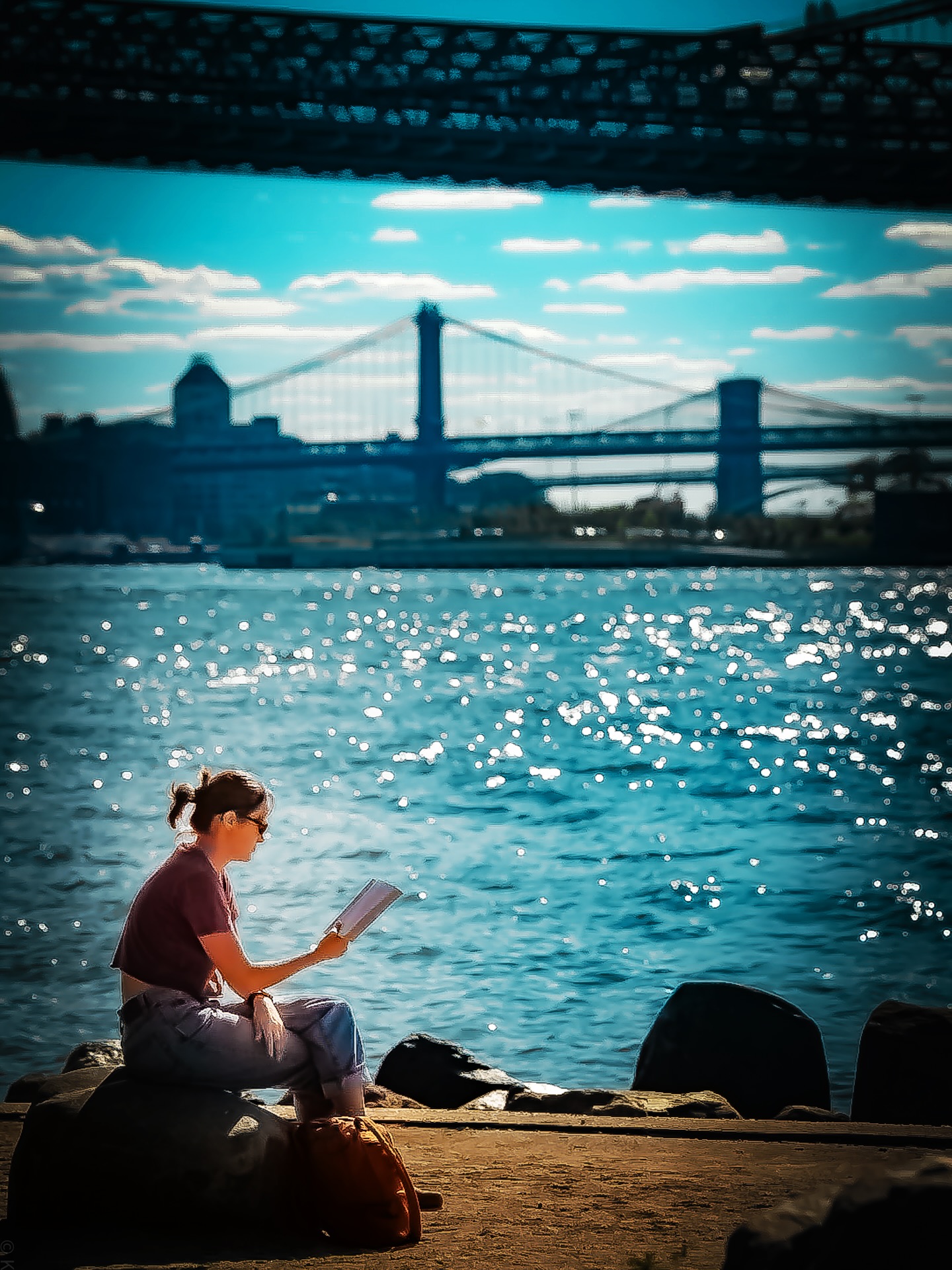 Reading by the river with a bridge behind